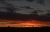 a sunset over a field with clouds in the background